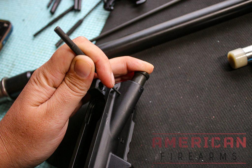 Using your middle finger to compress the forward assist, insert the roll pin into the hole and hammer it in.
