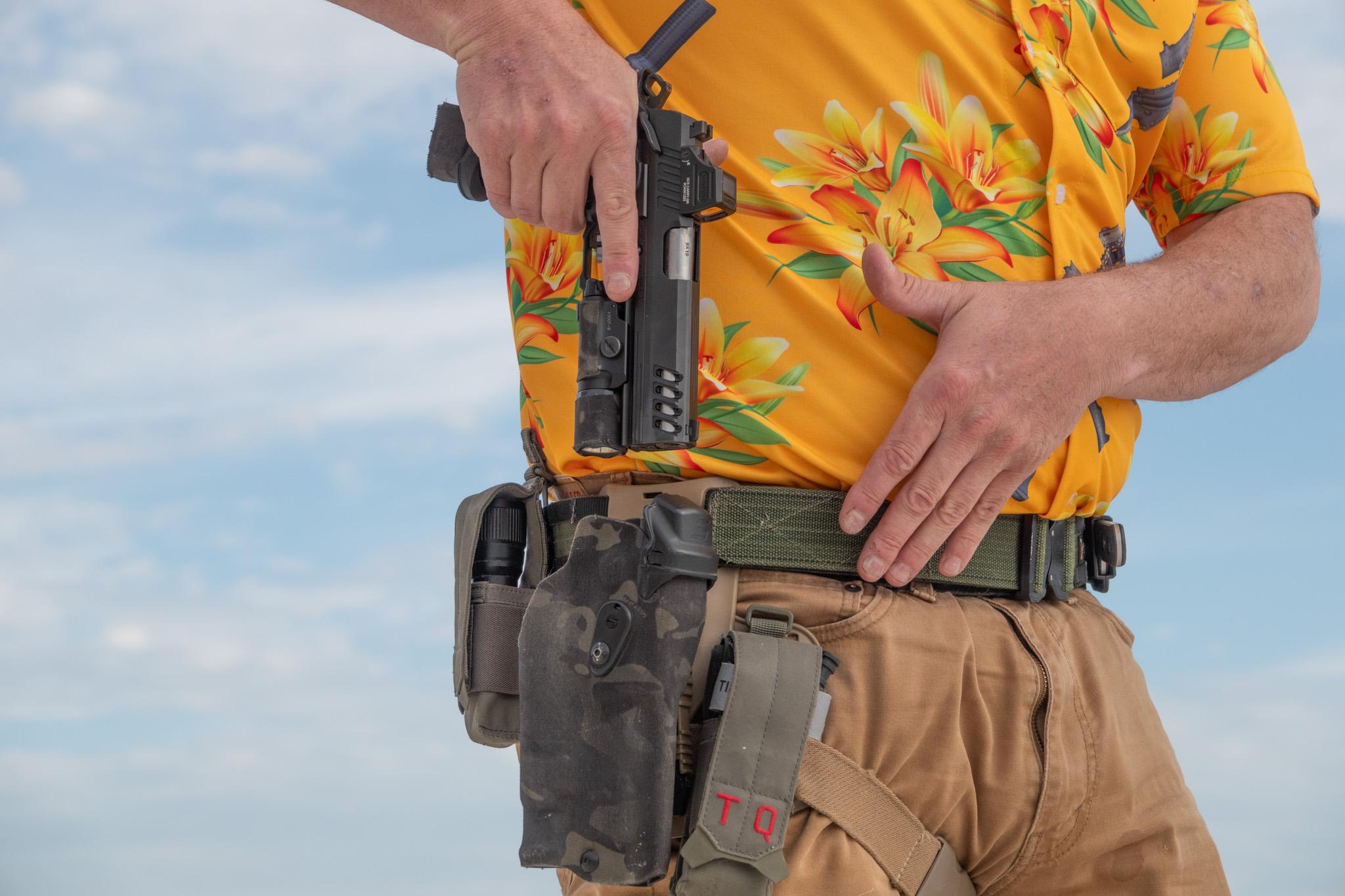 Reholstering the Bersa M2Xi in its camo Kydex holster, mounted on a battle belt alongside a tourniquet pouch and spare flashlight.